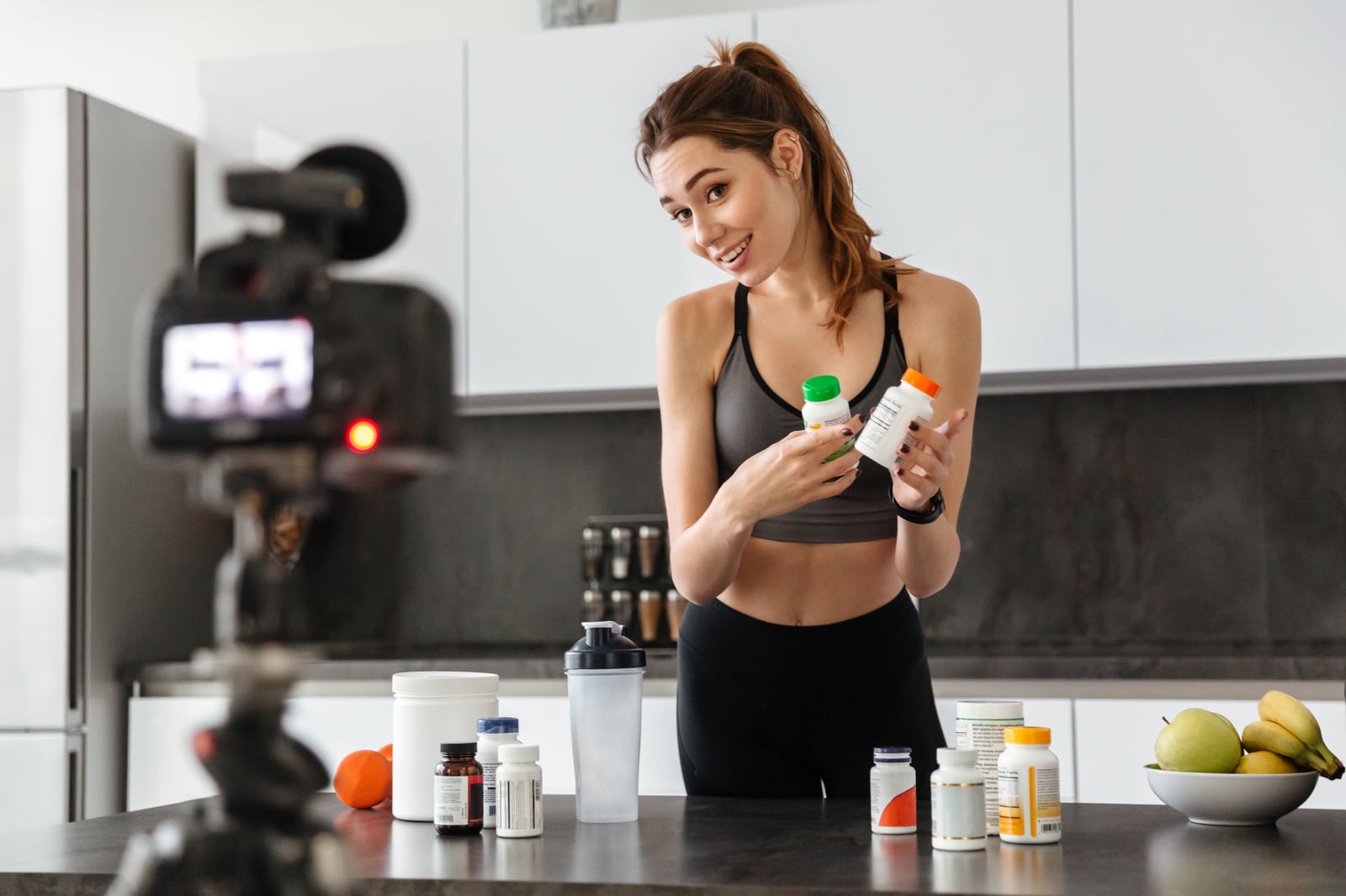 Criadora gravando um vídeo de produto em casa, segurando frascos de suplementos