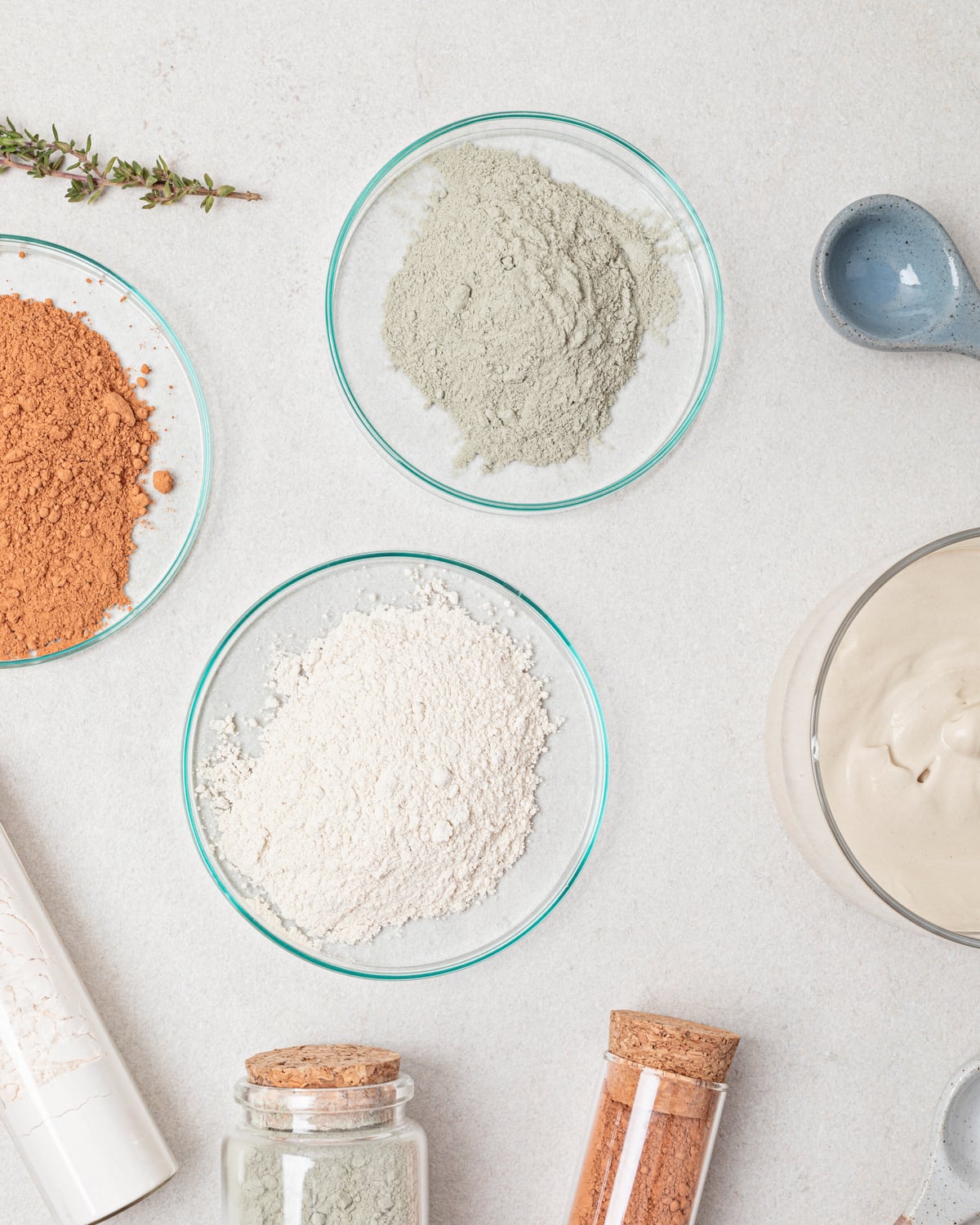 Loose supplement powders in glass dishes on a bone-coloured surface